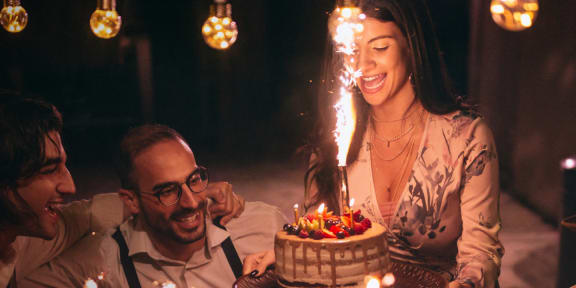 a group of people sitting around a table with a birthday cake with a lit candle