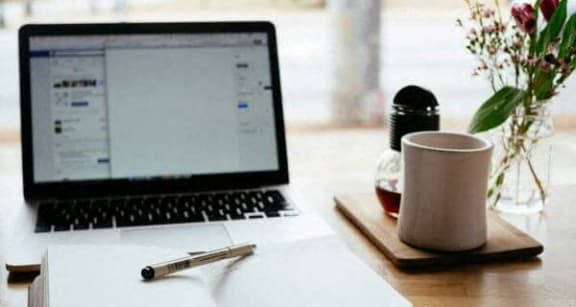 a laptop computer sitting on a desk with a notebook and a coffee cup
