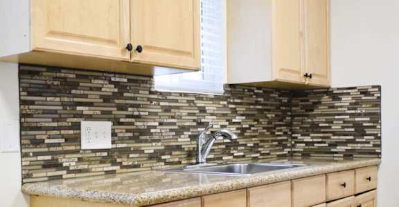 light wooden cabinets and tile backsplash with marble countertops