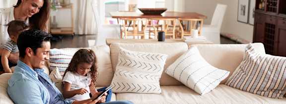 A family of three is sitting on a white couch in a living room.