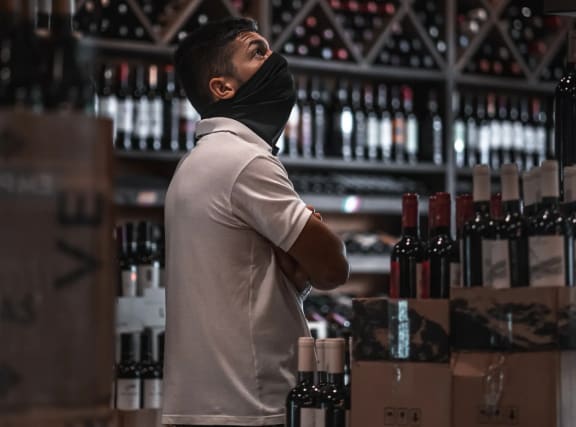 a man wearing a face mask standing in a wine bar with bottles