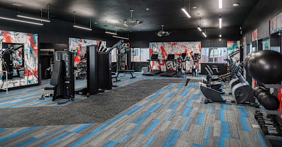a fitness room with weights and other exercise equipment and a wall of graffiti at Track 281 Apartments, Sacramento, 95811