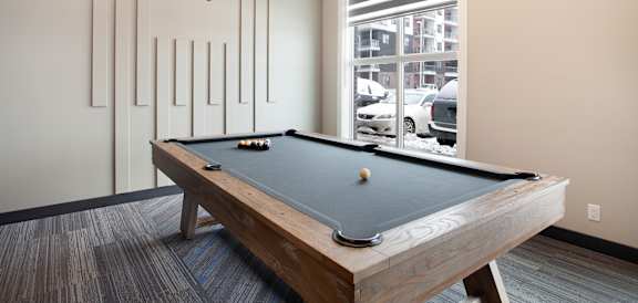 A pool table in a room with a window showing a parking lot outside.
