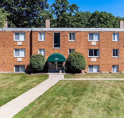 a brick apartment building with a green archway and a sidewalk