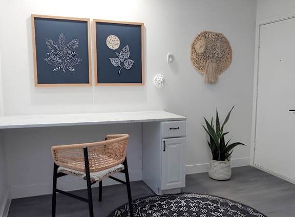 A room with a desk, chair, and two framed pictures on the wall.