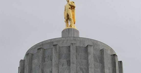A statue of a man stands on top of a grey building.