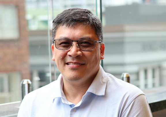 A woman in a grey suit stands in front of a framed picture of a boat.