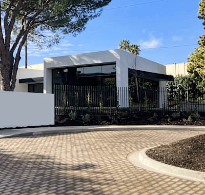 A modern house with a white fence and a large tree in front.