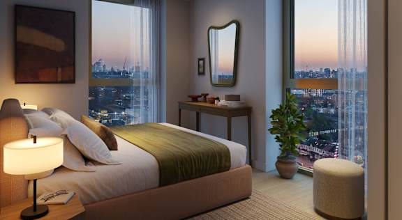 A bedroom with a large bed, a nightstand with a lamp, a mirror, and a window with a view of the city.