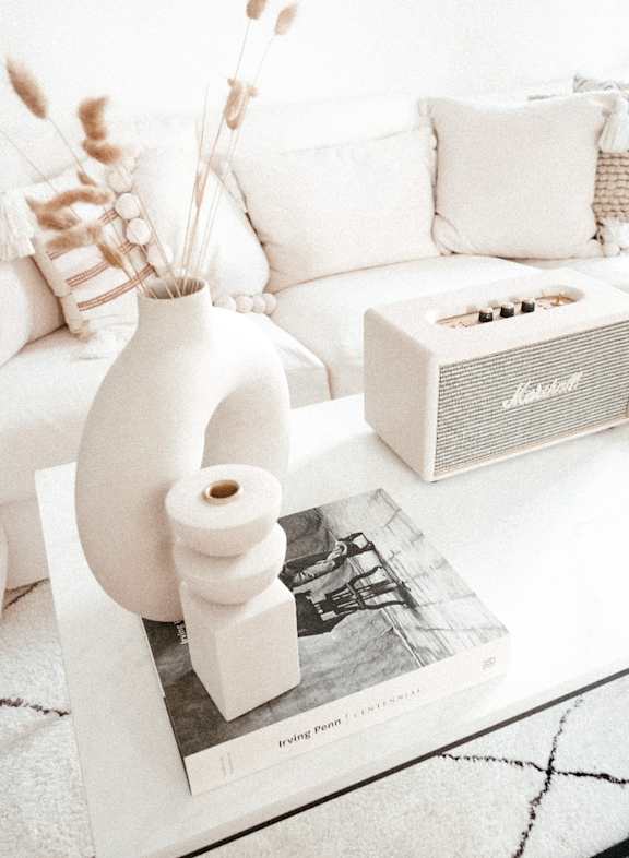 A cozy white sofa in an aesthetic living room, paired with a white coffee table and a white speaker.