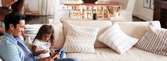 A family of three is sitting on a white couch in a living room.