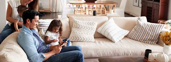 A family of three is sitting on a white couch in a living room.