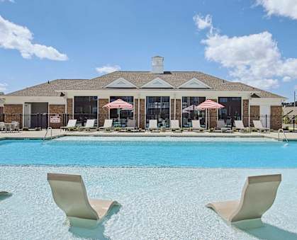 a large swimming pool with chairs and a building in the background