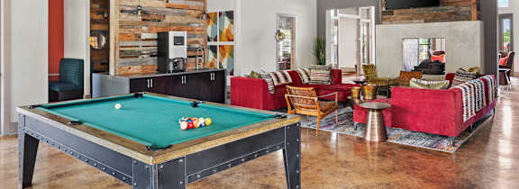 A pool table is in the middle of a room with a red couch and a television.