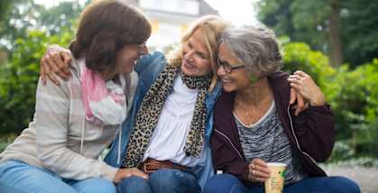 Three women sitting on a log in a wooded area.