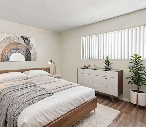 A bedroom with a large bed, a nightstand with a lamp, and a plant on the side table.