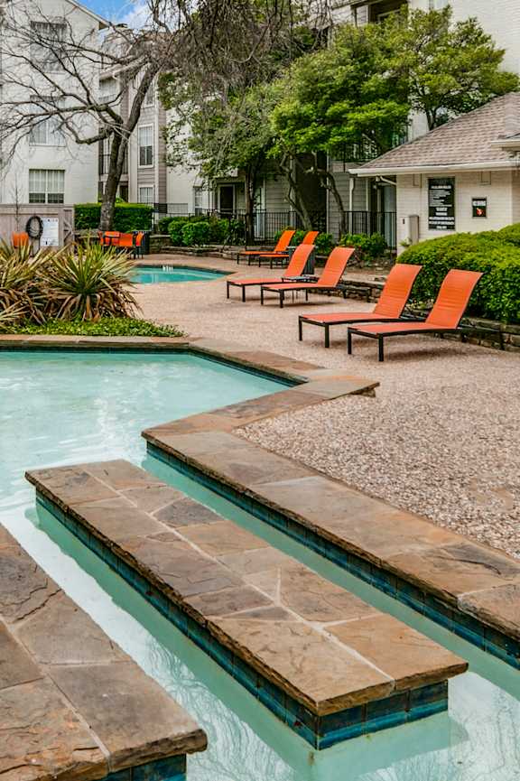 a swimming pool with orange chairs and a building in the background
