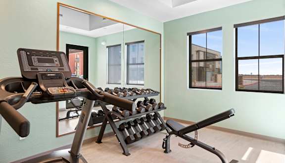 A gym room with a treadmill, weights, and mirrors.