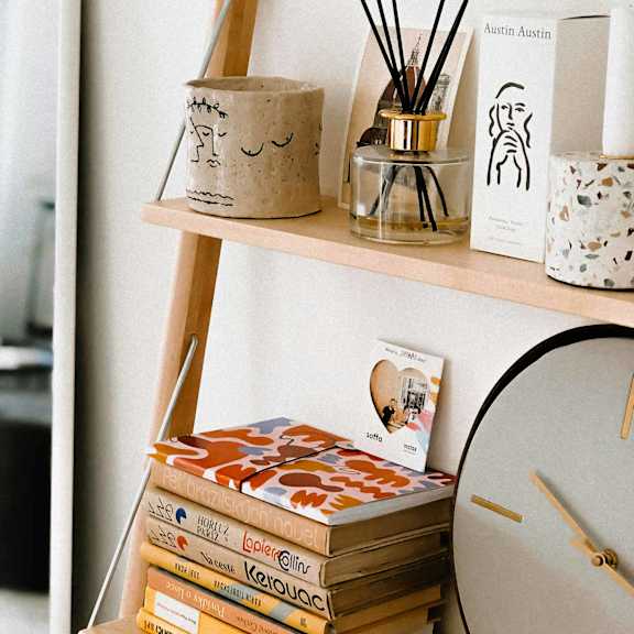 Interior decor of a shelf with books, a clock, and a diffuser.
