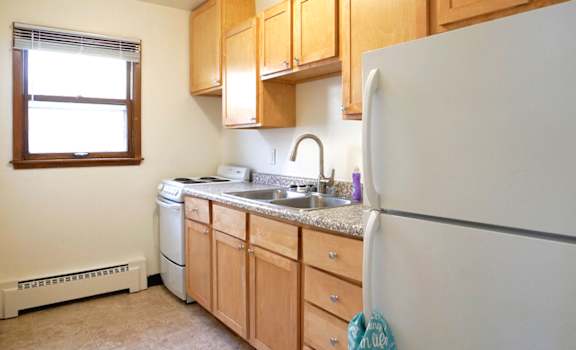 A kitchen with a white refrigerator, wooden cabinets, and a window.