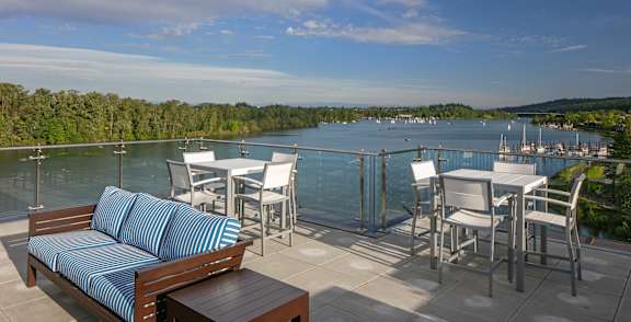 A wooden bench with blue cushions sits on a patio overlooking a river.
