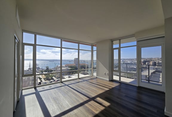 A large empty room with wooden floors and large windows overlooking a cityscape.