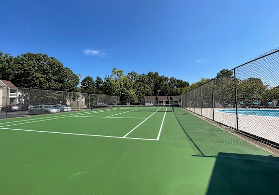 A tennis court surrounded by a fence with a clear blue sky above. at Lakes Edge Apartments, Greensboro, 27409