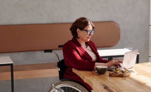 a woman in a wheelchair sitting at a table with a laptop