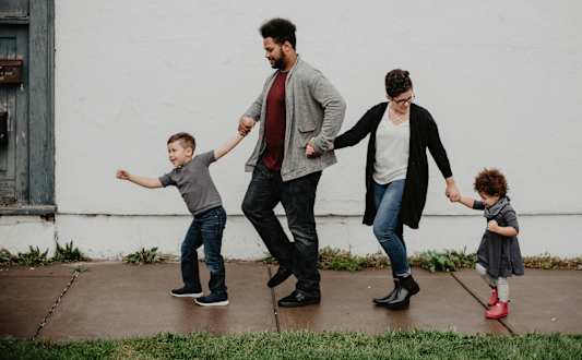 A family of four is walking together on a sidewalk.