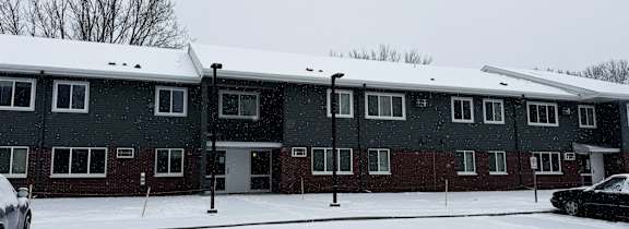 A black car is parked in front of a building with a snowy ground.