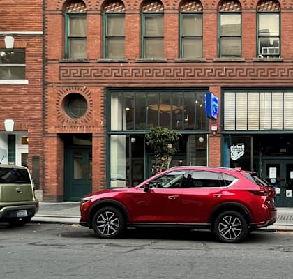 A red car is parked in front of a red brick building.