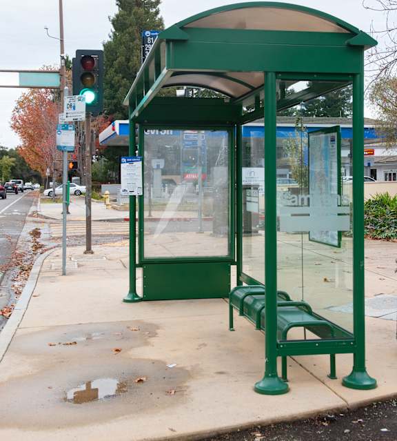 A green bus stop with a bench and a glass window.
