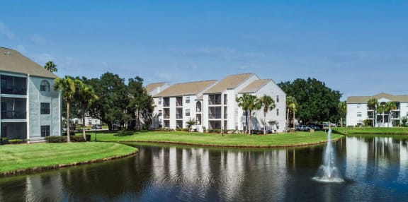 a fountain sits in the middle of a pond in front of apartment buildings