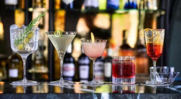 a row of different colored cocktails sitting on a bar