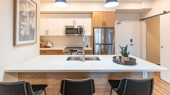 A modern kitchen with a white countertop and black chairs.