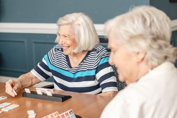 two older women sitting at a table playing a game of dominoes