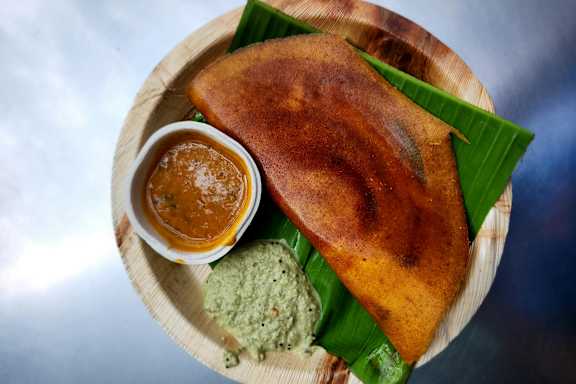 A plate of food with a dosa, chutney and sambar.