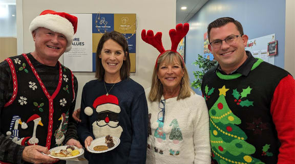 a group of people in ugly christmas sweaters holding plates of food