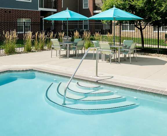 A pool with a slide and chairs around it.