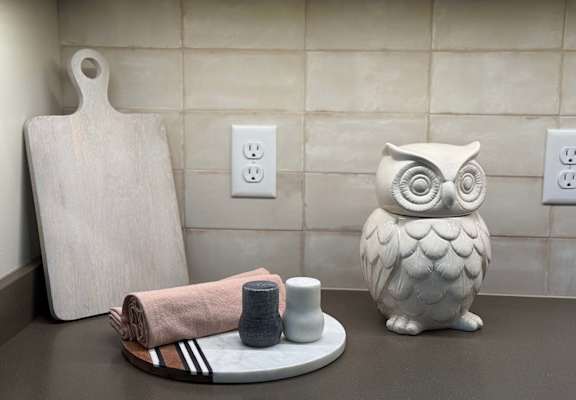a kitchen countertop decorated with a wooden cutting board, and owl statue, and a serving tray