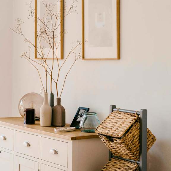 A white dresser with art above decorative accessories and a vase with branches on top of it.