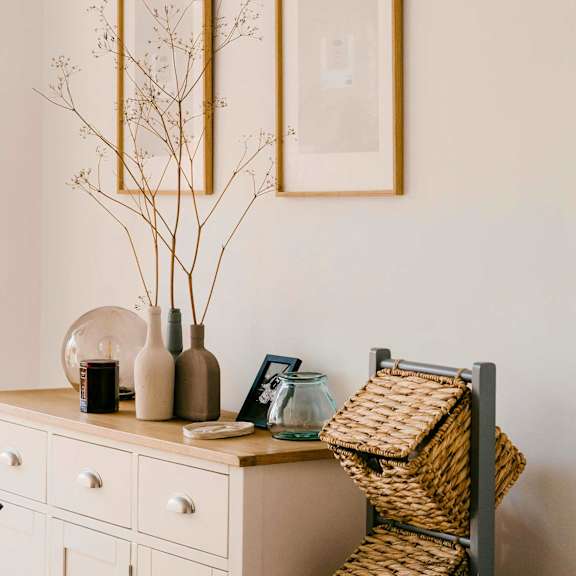 Entry decor of a white dresser holding pottery and a picture frame against a beige wall