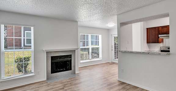an empty living room with a fireplace and a kitchen