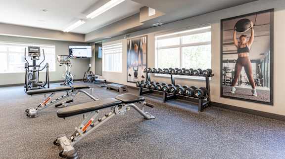 A spacious gym with a variety of equipment including dumbbells, weight plates, and a bench press.