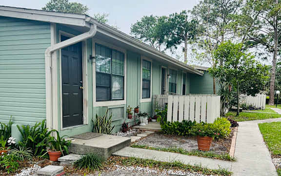 A green house with a white picket fence and a potted plant in front.
