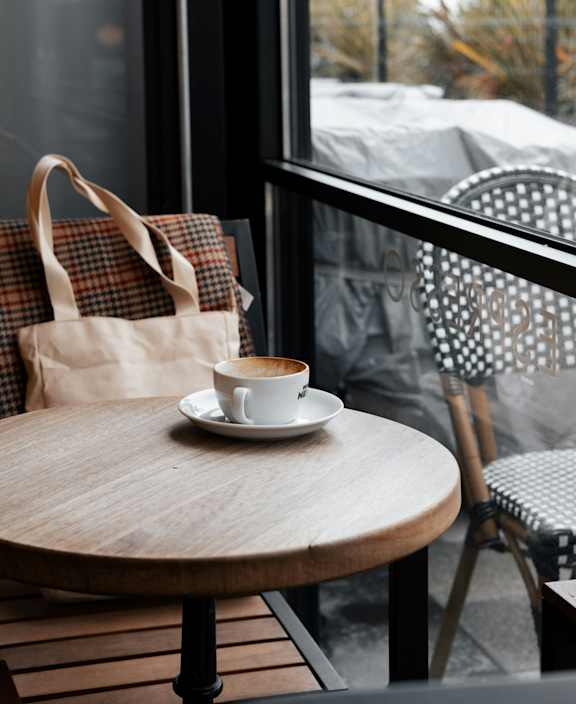A cup of coffee sits on a saucer on a wooden table.