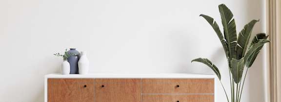 A white cabinet with a plant beside it.