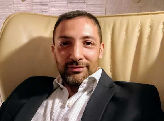 A man with a beard is wearing a black suit and a white shirt.