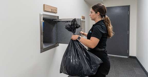 A woman is holding a black trash bag in front of a trash can at Podium Apartments, Calgary, AB
