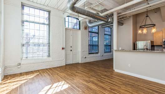 an open living room with wood flooring and exposed pipes and windows